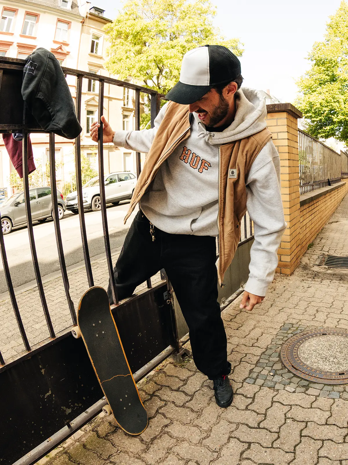 Levent Efe in huf® hoodie squeezing through a fence, laughing — ODD 7 behind the scenes, Frankfurt 2023 · Photo: Moritz Gasche